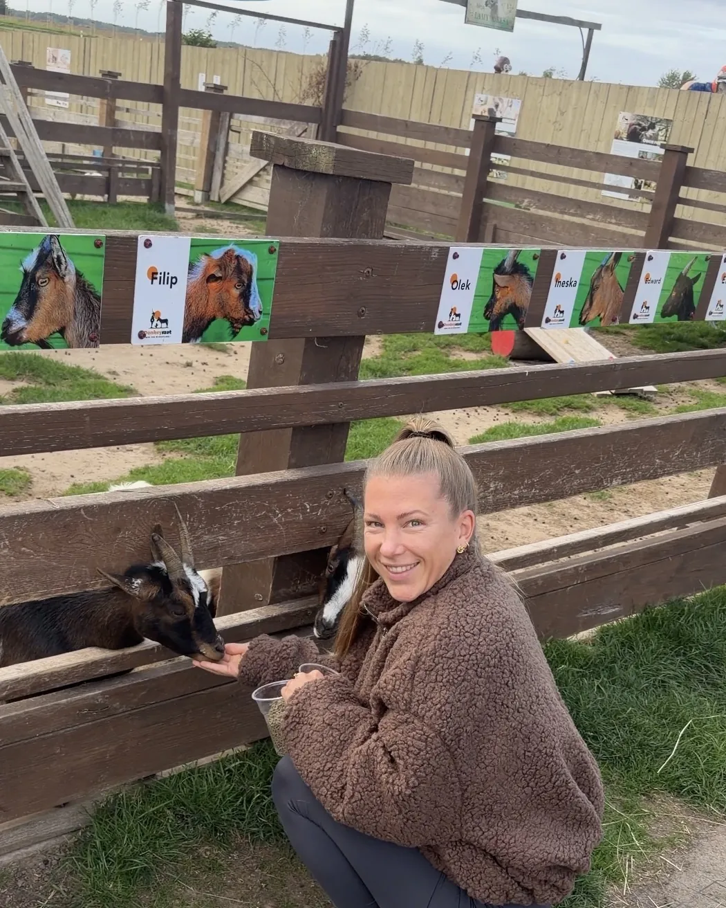 Helen Fritzsche hockt lächelnd an einem Holzzaun und füttert Ziegen